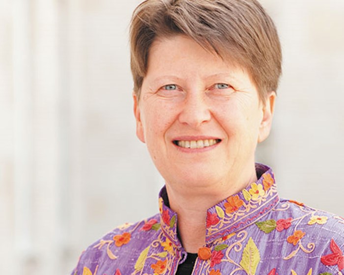 A headshot style image of a woman looking down a camera lens
