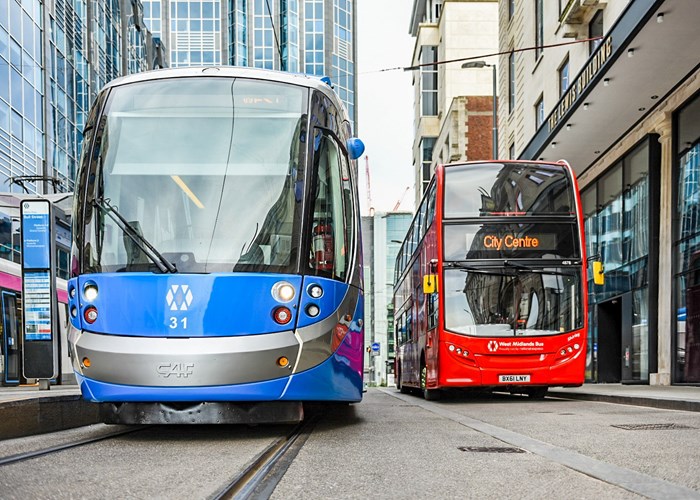 A West Midlands Metro blue tram alongside a red double decker bus in Birmingham