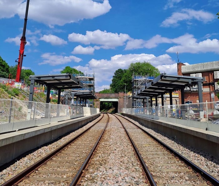 Standing on twin railway track looking along the platforms either side with new canopies installed and a large crane on the left