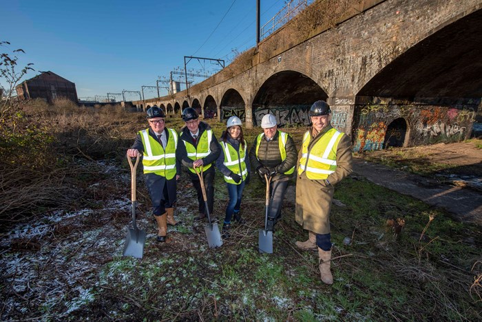 Five people in high-vis yellow vests and hard hats in front of the large historic railway viaduct