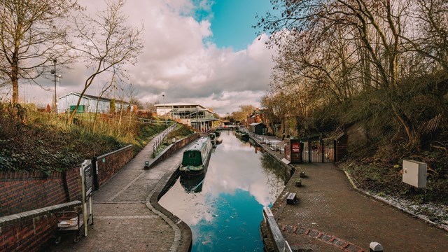Canal with a narrow boat, walk way and cloudy sky in the background