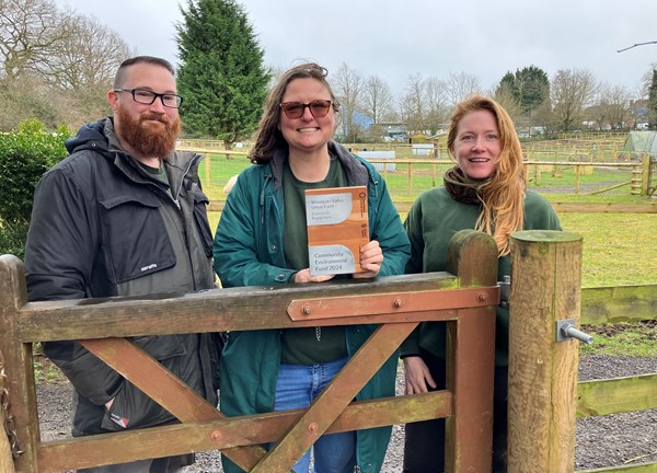 3 people at a farm holding a brochure and smiling to the camera