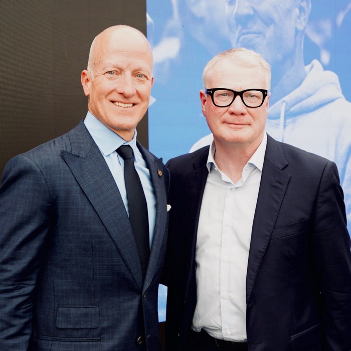Two men stand side to side smiling at the camera